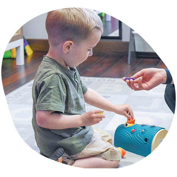 a young blonde boy wearing a green shirt and beige shorts playing with a puzzle toy.